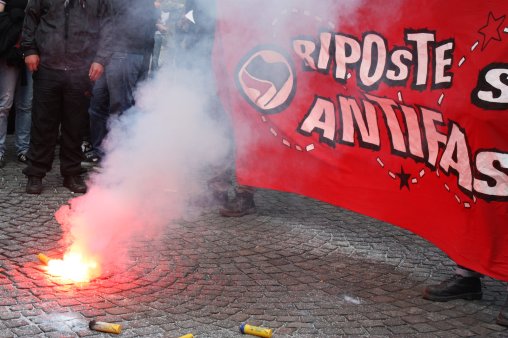 Image d'un fumigène devant une banderolle Riposte Antifa